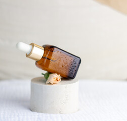 An elegant bottle in noble dark glass with natural serum and the most delicate cream to brighten your skin is decorated with an elegant flower on a plaster catwalk.