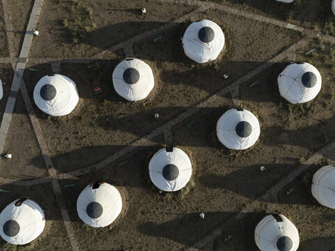 Aerial view of a cluster of traditional white yurts casting long shadows on the arid, brown landscape, creating a stark contrast of light and shade, Turgen, Uvs, Mongolia.
