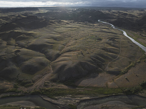 Aerial view of the rugged, undulating terrain where sunlight dances across the hills and the river winds its way through the landscape, Turgen, Uvs, Mongolia.