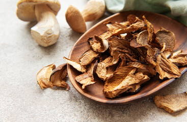 Dried porcini mushrooms resting in wooden bowl on gray textured background
