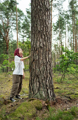 Young woman touching a large tree trunk in a pine forest, admiring nature