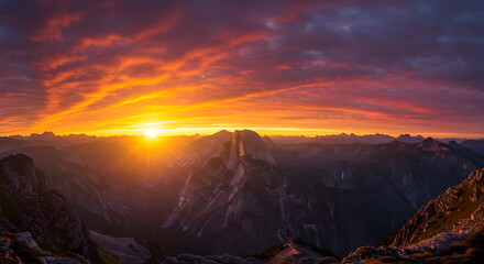 Naklejka premium Panoramic vista of a rugged mountain range bathed in the radiant glow of a fiery dawn over the misty valley peaks