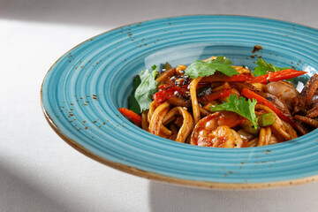 Korean udon noodle dish with shrimp, squid, red pepper and fresh herbs served in a rustic blue plate on white background