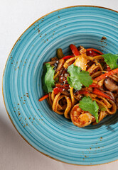 Korean udon noodle dish with shrimp, squid, red pepper and fresh herbs served in a rustic blue plate on white background