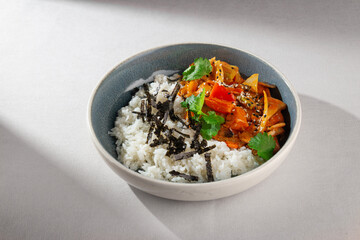 Traditional Korean rice bowl with kimchi-based stew, vegetables, sesame seeds, cilantro and shredded seaweed served in a ceramic bowl on white background