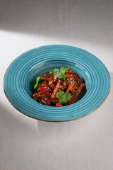 Traditional Korean japchae noodles with beef, bell pepper, carrot, sesame seeds and cilantro served in a rustic blue ceramic plate on white background