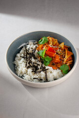 Traditional Korean rice bowl with kimchi-based stew, vegetables, sesame seeds, cilantro and shredded seaweed served in a ceramic bowl on white background