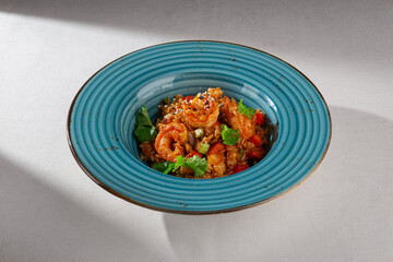 Spicy Korean style kimchi fried rice with shrimp, bell pepper, sesame seeds and fresh cilantro served in a rustic blue ceramic bowl on white background
