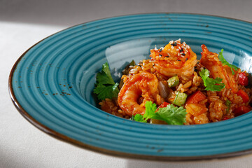 Spicy Korean style kimchi fried rice with shrimp, bell pepper, sesame seeds and fresh cilantro served in a rustic blue ceramic bowl on white background