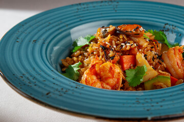 Spicy Korean style kimchi fried rice with shrimp, bell pepper, sesame seeds and fresh cilantro served in a rustic blue ceramic bowl on white background
