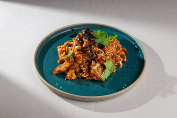 Spicy Korean style kimchi fried rice with chicken, shredded seaweed, sesame seeds and cilantro served on a rustic blue ceramic plate over white background