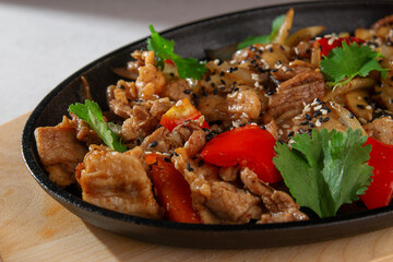 Traditional Korean style grilled pork with bell peppers, onions, sesame seeds and fresh cilantro served on a sizzling hot plate over wooden board