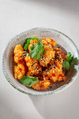 Crispy Korean chicken bites coated in glossy sweet chili sauce, sprinkled with sesame seeds and garnished with cilantro, served in a rustic ceramic bowl
