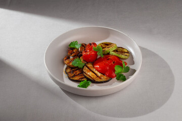 A mix of grilled vegetables including eggplant, zucchini and red bell pepper, garnished with fresh cilantro and served on a clean white ceramic plate