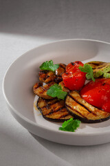 A mix of grilled vegetables including eggplant, zucchini and red bell pepper, garnished with fresh cilantro and served on a clean white ceramic plate