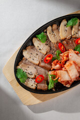 Sliced pork belly served on cast iron plate with traditional Korean kimchi, fresh cilantro, black sesame seeds and red chili peppers for garnish