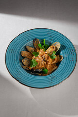 Cooked mussels in shells served with a rich spicy creamy sauce and fresh herbs in a rustic blue bowl on a light tablecloth, top-down view