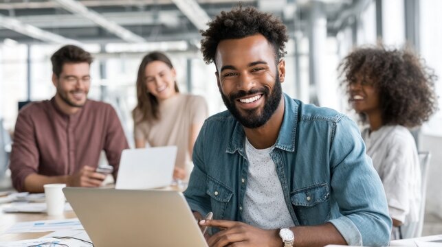 Young businessman smiling and working with laptop in modern office with colleagues