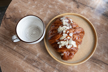 A croissant resting on a plate next to a cup of coffee