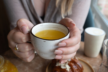 A woman is carefully holding a cup that contains yellow liquid