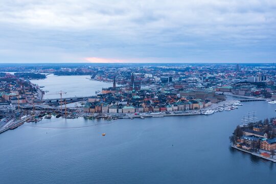 Aerial view of the shimmering water weaving through Stockholm's islands, crowned by historic buildings and the distant glow of the setting sun, Stockholm, Stockholm County, Sweden.