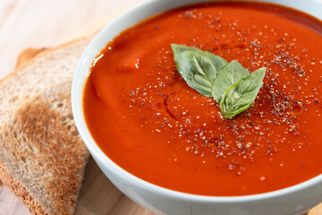 Homemade Tomato Soup in bowl with Basil on rustic wooden table