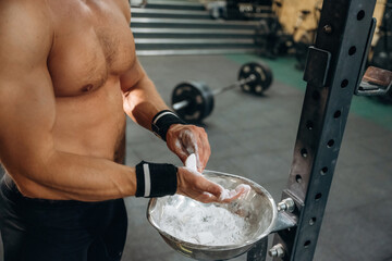 Preparing for competition. Fitness man is rubbing his hands with chalk, specifically magnesium...