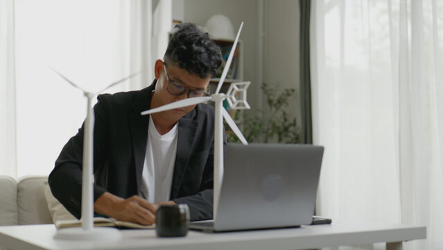 Asian businessman carefully inspecting a miniature wind turbine model made from recycled plastic. - Powered by Adobe