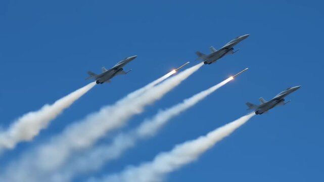 Four fighter jets performing a synchronized aerial maneuver, releasing flares against a clear blue sky