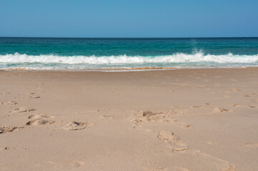 Turquoise ocean waves crashing on sandy beach paradise during the day with blue sky.