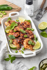 Spicy grilled chicken thighs roasted with chilli and lime on white dish, light gray kitchen background