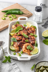 Spicy grilled chicken thighs roasted with chilli and lime on white dish, light gray kitchen background