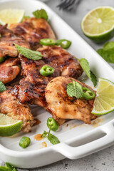 Spicy grilled chicken thighs roasted with chilli and lime on white dish close up, light gray kitchen background