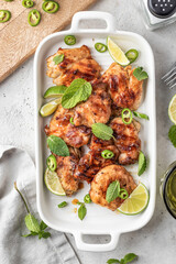 Spicy grilled chicken thighs roasted with chilli and lime on white dish, light gray kitchen background top view