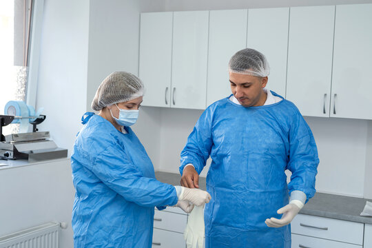 female assistant helping put on sterile clothes male surgeon in an operating room.  Hygiene or safety