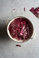 Shredded radicchio in a colander on a stone surface, seen from overhead.