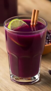 Glass of traditional peruvian chicha morada with a lime wedge and a cinnamon stick garnish