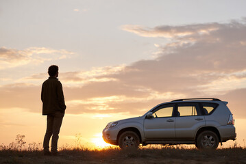 Silhouette of traveler standing next to SUV at sunset in desert.