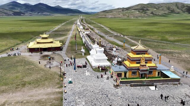 Aerial view of the golden roofed buildings and white stupas alongside the Bage Mani Stone Wall, contrasting with the green meadows, Bage, Sichuan, China.