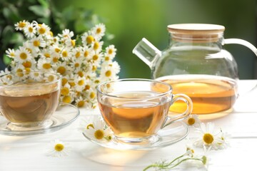 Aromatic tea in glass cups and chamomile flowers on white wooden table, closeup