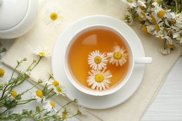 Tasty chamomile tea and flowers on white wooden table, flat lay