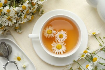 Tasty chamomile tea, infuser and flowers on white wooden table, flat lay