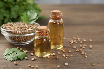 Aromatic oil in bottles, cilantro leaves and coriander seeds on wooden table, closeup