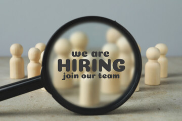 We are hiring, join our team. Magnifying glass with inscription inside against human figures on grey table