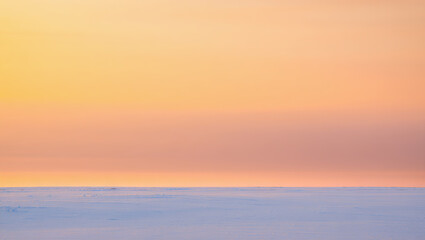 Fototapeta premium Soft pastel colors fill the sky as the sun sets over a vast, snowy horizon in a tranquil winter landscape. This peaceful scene invites reflection and calm