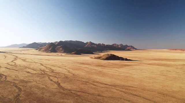 Aerial view of a vast, arid landscape with rocky mountains under a clear blue sky, creating a striking contrast of textures and tones, D707, Karas Region, Namibia.