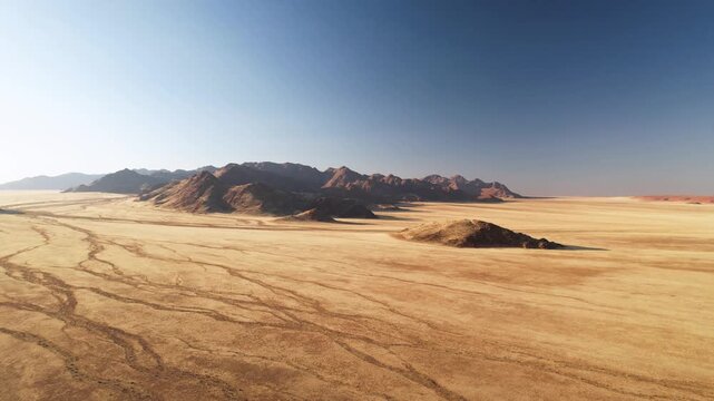 Aerial view of a vast desert landscape stretching to the horizon, with rugged mountains providing a stark contrast against the clear blue sky, D707, Karas Region, Namibia.