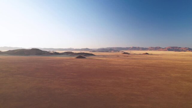 Aerial view of the vast Namib desert landscape with arid plains and distant mountains under a clear blue sky, D707, Karas Region, Namibia.