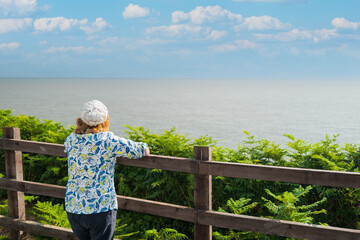 Woman at a British holiday resort looking out to the sea. The fence is located at the top of a steep cliff edge.