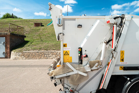 Abstract view of the rear of a new waste management vehicle seen on a British promenade. The various control buttons and warning signs are clearly visible on the collector.